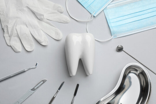 Tooth shaped holder, set of different dentist's tools, face masks and gloves on light grey background, flat lay
