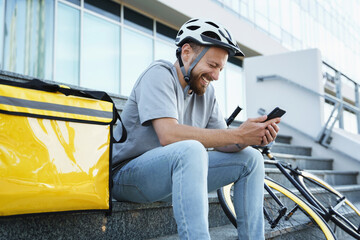 Express food delivery courier sitting on the stairs with insulated bag and bicycle.