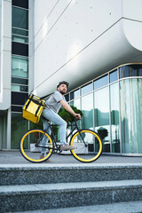 Express delivery courier standing on bicycle with insulated bag.