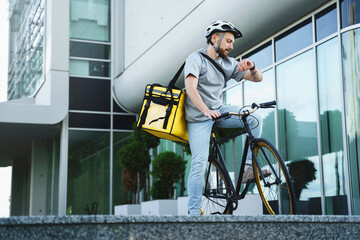 Express delivery courier with insulated bag looking at watch on bicycle.