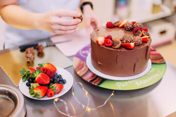 chef girl cooks chocolate cake with strawberries. the pastry chef puts the berries on the cake. a pastry chef decorates a chocolate cake with berries (strawberries, blueberries) and sweets