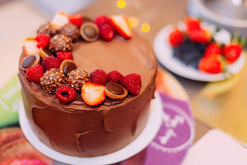 Chocolate cake decorated with fresh berries (strawberries, blueberries) on a white stand