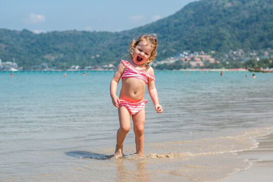 a little girl with curly hair is playing, laughing, rejoicing on the seashore. a child is playing on a sandy beach. happy childhood. summer holidays. kids and the sea