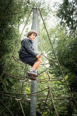 Boy sitting on rope frame in playground
