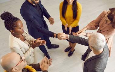 Successful young man receives gratitude, appreciation and recognition among coworkers. Happy businessman exchanges handshake with business executive while multiethnic team of people are clapping hands