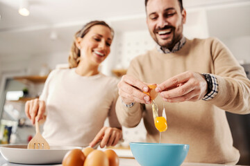 Close up of a man breaking the egg in the kitchen. Couple preparing breakfast together.