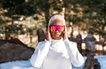 African American woman standing with sunglasses in a snowy park during winter