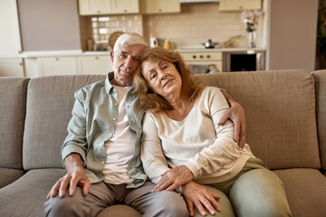 Elderly couple sit on sofa and look at camera