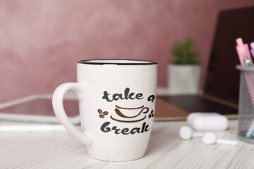 Cup of coffee with inscription Take a Break on white wooden table in office