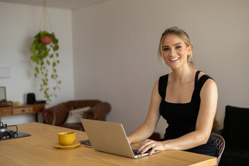 Young woman working at home in her kitchen with laptop and papers on kitchen wooden desk. Home office concept.