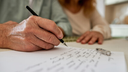 Man writing letter on paper near his blurred wife