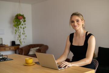 Young woman working at home in her kitchen with laptop and papers on kitchen wooden desk. Home office concept.