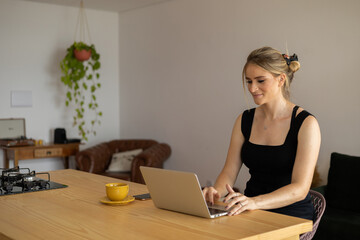 Young woman working at home in her kitchen with laptop and papers on kitchen wooden desk. Home office concept.