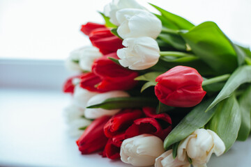 A beautiful bouquet of spring flowers of tulips of red and white color lies on the windowsill/