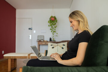Young woman working at home from her living room couch with laptop on her lap. Home office concept.