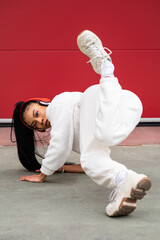 Cheerful African American woman with headphones dancing urban dance on a red background