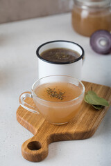 Homemade bone broth in mugs with spices on a wooden stick with bay leaf.