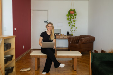 Young woman working at home from her living room couch with laptop on her lap. Home office concept.