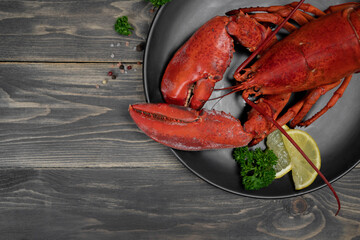 Lobster decorated with lemon slices on black plate on wooden table. Fresh seafood.