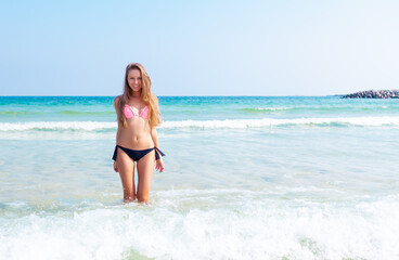 Fototapeta na wymiar Young attractive blonde girl with perfect sport body in bikini on the tropical summer beach