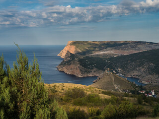 Dawn in the mountains. View of the mountain, sea, sky, clouds, below in the distance you can see the city of Balaklava with a fortress. Crimea. Mountain landscape. Beautiful wallpaper.