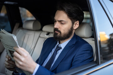 A handsome young businessman in a suit outdoors using his mobile phone is driving in the car