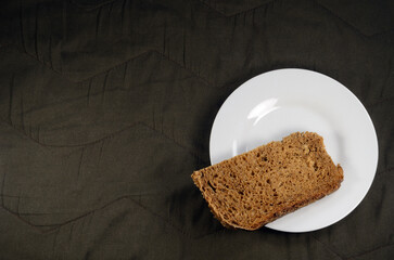 Fresh rye bread on a white saucer, brown fabric background.