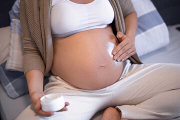 A beautiful young pregnant woman is putting lotion on to her belly