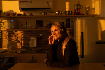 Young woman listening to music with headphones in her ears in the kitchen of her apartment. High quality photo.