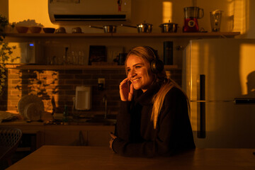 Young woman listening to music with headphones in her ears in the kitchen of her apartment. High quality photo.