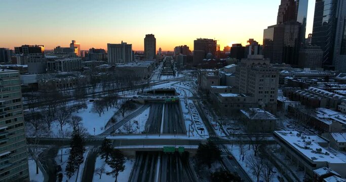 Urban city in USA. Silhouette of buildings at sunrise in winter snow scene in America. Aerial above highway.