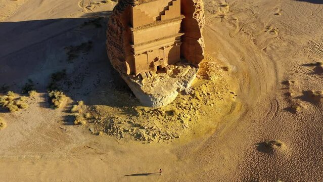 Aerial view of a man in front of the Hegra monument, in Mada'in Saleh, Saudi Arabia - reverse, tilt, drone shot