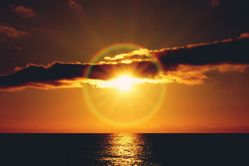 Rainbow halo around the sun at sunset, over the Atlantic Ocean, captured from a beach in Tenerife,...