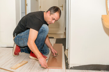 Working man with amputated fingers. He is working on laying the flooring in his house during the day.