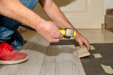 Hammer handle held by the hand with two amputated fingers of a person with dirty slippers as he works laying floors in his house.