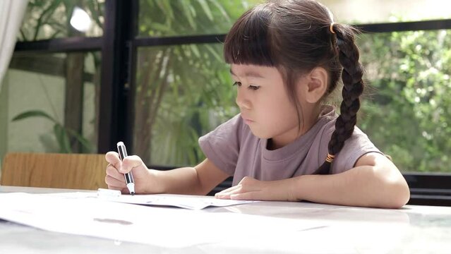 cute little asian girl sitting on the table Drawing and coloring on paper at home. Children's education concepts. online learning from home