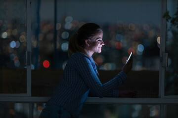 Young woman using a smartphone at night time with city view landscape in the background. High quality photo