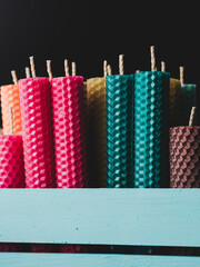 Many multi-colored beeswax candles with honeycomb texture are in a blue wooden box.