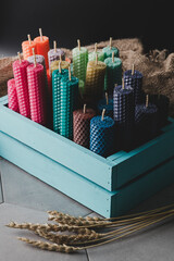 Many multi-colored beeswax candles with honeycomb texture are in a blue wooden box.