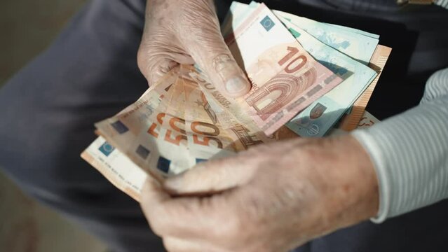 Pensioner in despair counting his miserable pension income, grandfather holding euro paper currency in his wrinkled hands sitting on the chair. Problem of poverty during world financial inflation
