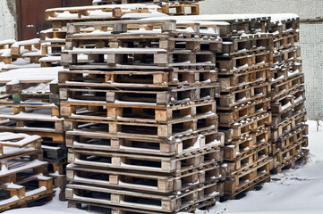 Many used, but still whole pallets are stacked outdoors, wooden pallets, snow lies on them, winter has come