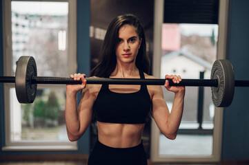 Naklejka na ściany i meble Beautiful athletic woman lifting barbell while training in the gym