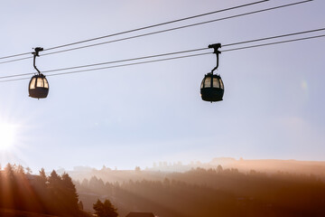 Two cable car cabins in the air and rising sun over Seiser Alm plateau covered in morning haze