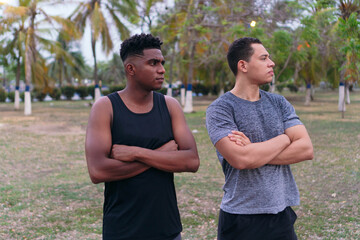 Two men in sportswear, standing in a park, smiling with their arms crossed.