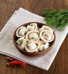 Bowl with freshly boiled meat dumplings, dill and chili pepper on wooden table background.