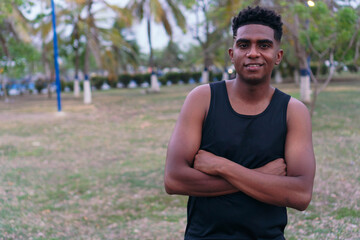 African man in sportswear, standing in a park, smiling with his arms crossed.