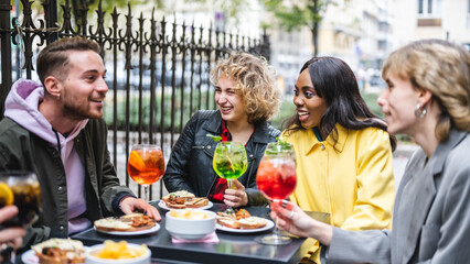 Multiracial happy young friends eating and drinking, diverse cheerful mates laughing enjoying meal, having fun sitting together at restaurant table