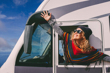 Overjoyed young adult woman oustretching arms outside the windows of a camper van and celebrate...