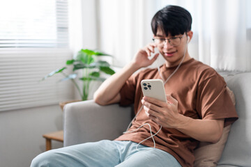 Technology Concept The person who wears glasses and headphones sitting on the grey couch and listening music on his smartphone