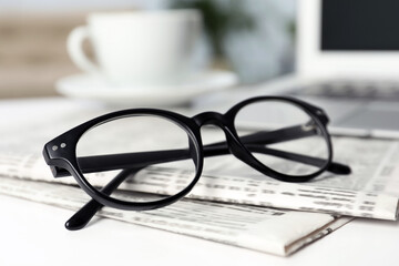 Newspapers and glasses on white table indoors, closeup